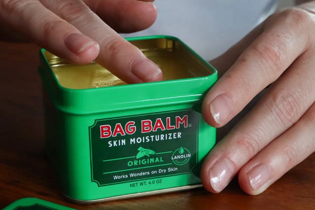 <p>A hand dips into a tin of Vermont’s Original Bag Balm skin moisturizer</p>